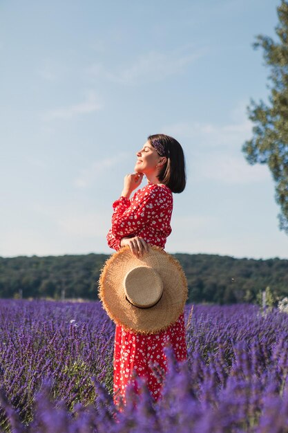 Giovane donna in piedi in un campo di lavanda e in possesso di un cappello di paglia