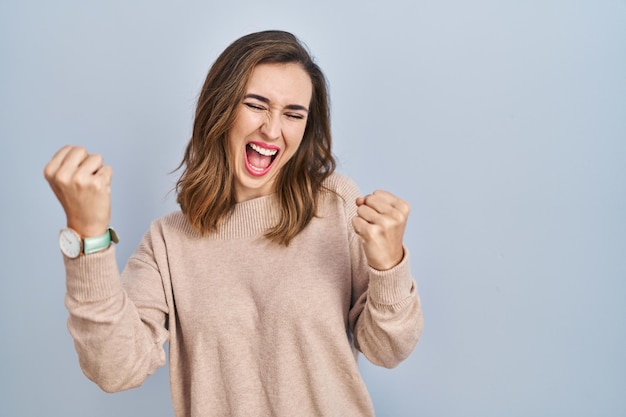 Giovane donna in piedi su sfondo isolato molto felice ed eccitato facendo il gesto del vincitore con le braccia alzate, sorridendo e urlando per il successo. concetto di celebrazione.