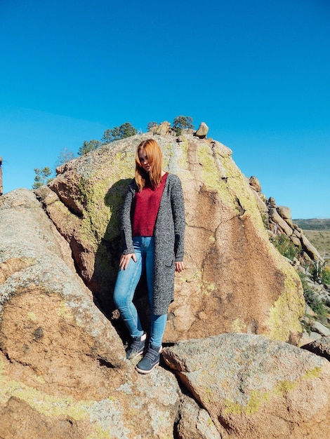 Giovane donna in piedi su una roccia contro il cielo blu
