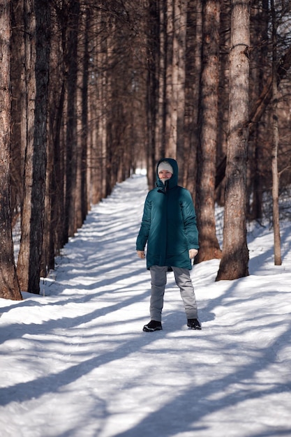Giovane donna in piedi sulla strada tra gli alberi donna caucasica cammina in una giornata gelida di sole nella foresta dopo pesanti...