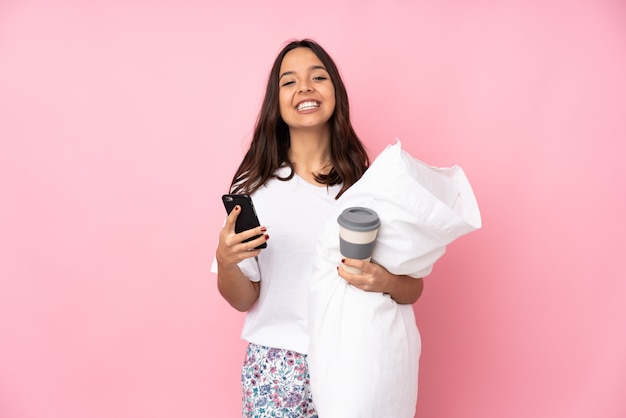 Giovane donna in pigiama sul muro rosa tenendo il caffè da portare via e un cellulare