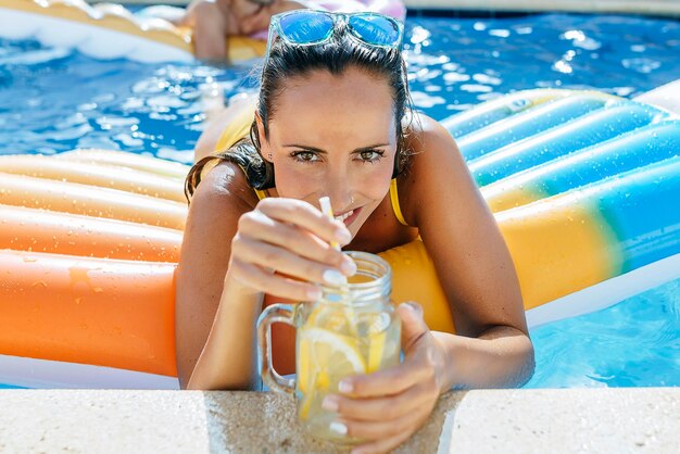 Giovane donna in piscina con drink a bordo piscina