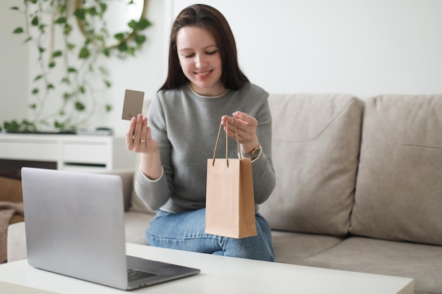 Giovane donna in possesso di carta di credito e utilizzando il computer portatile a casa Pagare online shopping domestico banca Internet negozio elettronico concetto