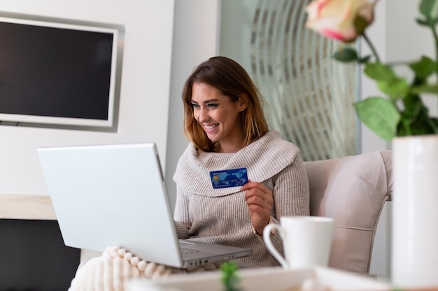 Giovane donna in possesso di carta di credito e utilizzando il computer portatile. Concetto di acquisto online. Donna felice che fa shopping online a casa