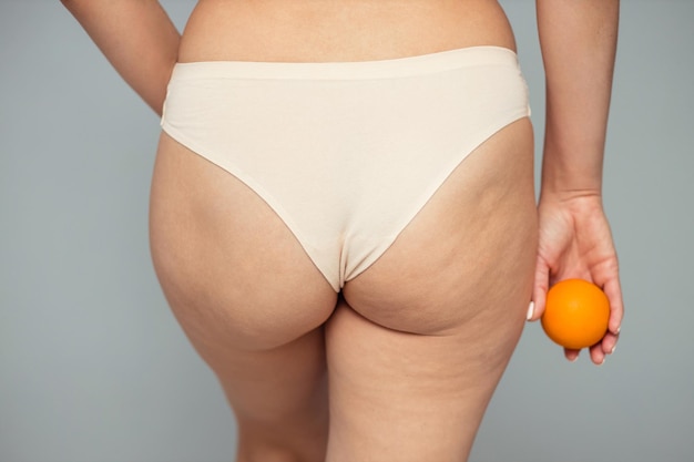 Giovane donna in possesso di un arancione su sfondo chiaro Concetto di problema di cellulite