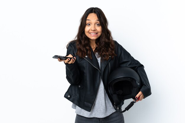 Giovane donna in possesso di un casco da motociclista su sfondo bianco isolato mantenendo una conversazione con il telefono cellulare con qualcuno