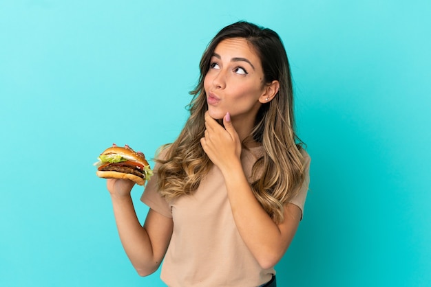 Giovane donna in possesso di un hamburger su sfondo isolato e guardando in alto