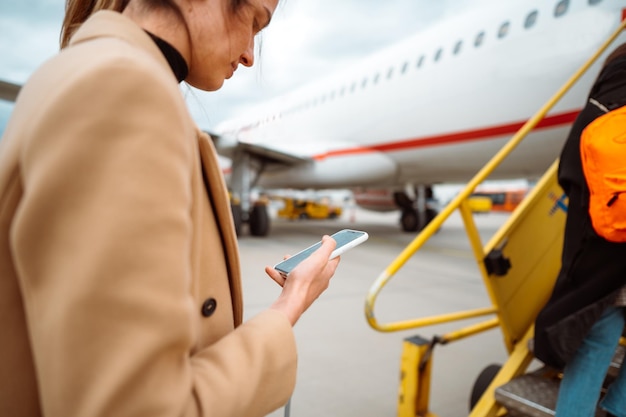 Giovane donna in possesso di un telefono cellulare e la scrittura di un messaggio Imbarco sull'aereo Primo viaggio dopo