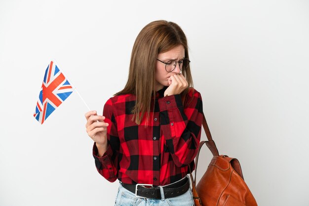 Giovane donna in possesso di una bandiera del Regno Unito isolata su sfondo blu con dubbi