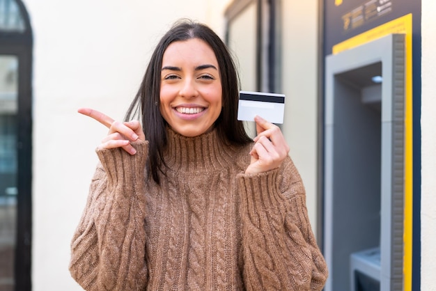 Giovane donna in possesso di una carta di credito all'aperto sorpresa e puntando il dito di lato