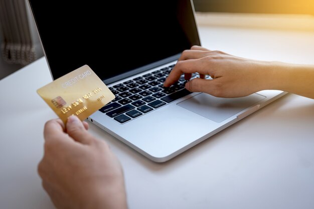 Giovane donna in possesso di una carta di credito e digitando su un computer portatile