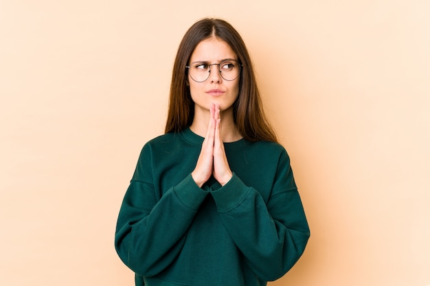 Giovane donna in preghiera beige, mostrando devozione, persona religiosa in cerca di ispirazione divina.