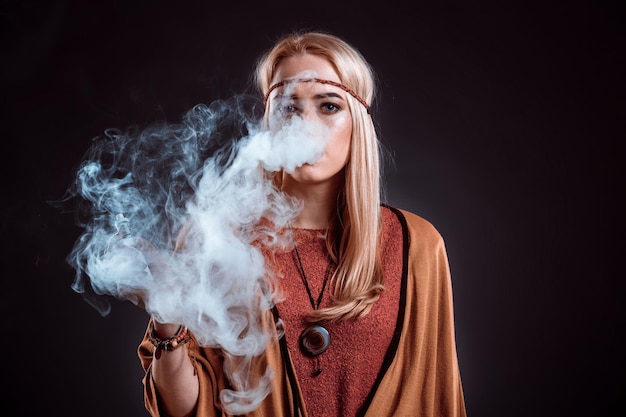 Giovane donna in stile boho che soffia fumo