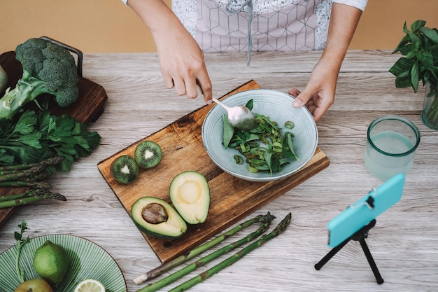 Giovane donna in streaming online lezione di cucina di cibi sani di insalata verde con frutta e verdura - Focus sulla mano destra