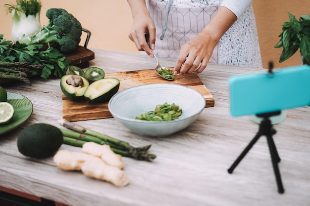 Giovane donna in streaming online lezione di cucina di cibi sani di insalata verde con frutta e verdura - Focus sulla mano destra