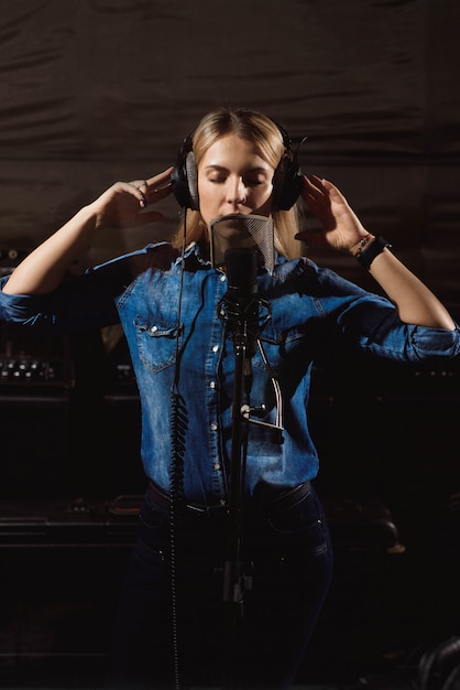 Giovane donna in studio di registrazione che parla nel microfono.