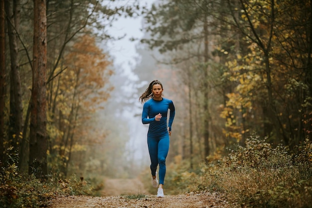 Giovane donna in tuta blu che corre verso la telecamera sul sentiero nel bosco in autunno