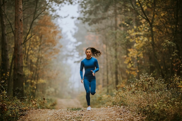 Giovane donna in tuta blu che corre verso la telecamera sul sentiero nel bosco in autunno