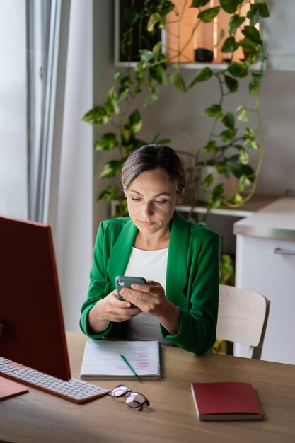 Giovane donna in ufficio a casa che utilizza smartphone con i social network Luogo di lavoro accogliente con ampia finestra