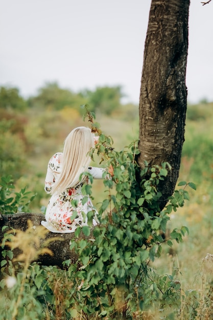 Giovane donna in un abito floreale seduto su un albero