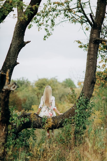 Giovane donna in un abito floreale seduto su un albero
