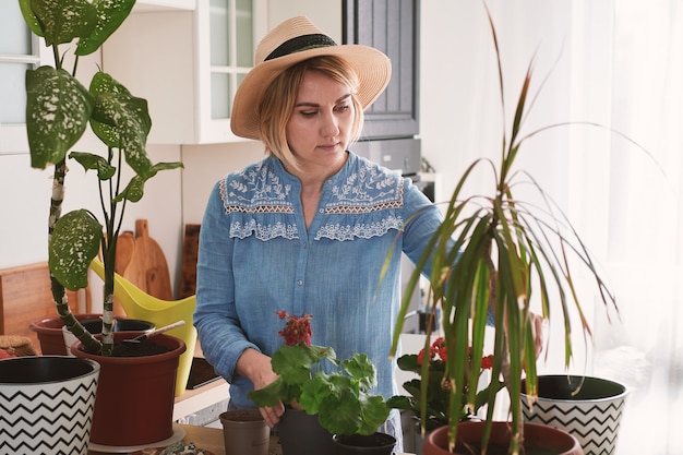Giovane donna in un cappello di paglia che cresce e pianta i fiori domestici