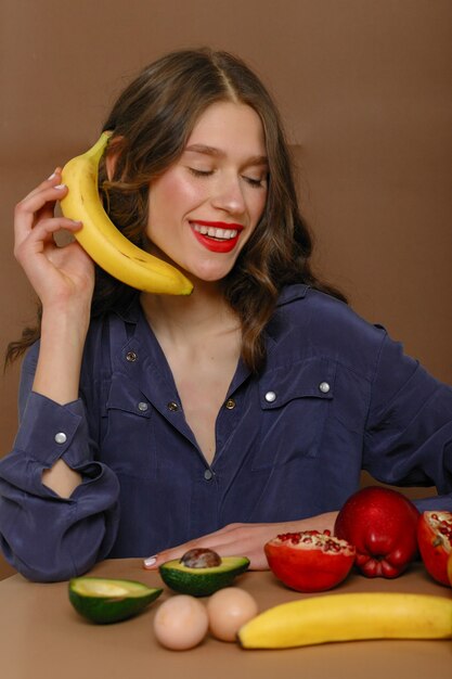 Giovane donna in un gruppo di frutta. Sanità e concetto di alimentazione sana. si siede parla in una banana come un telefono