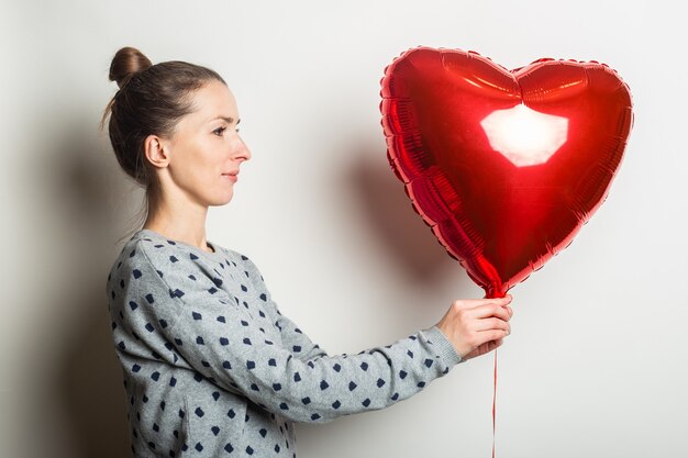 Giovane donna in un maglione guarda la mongolfiera cuore su uno sfondo chiaro. San Valentino concetto.