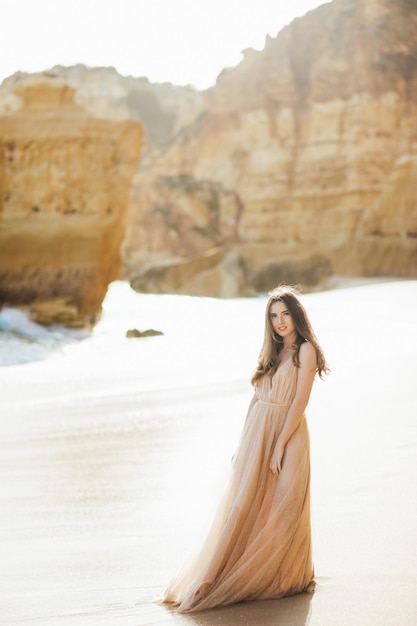giovane donna in un vestito lungo che cammina sulla spiaggia vicino all'oceano.