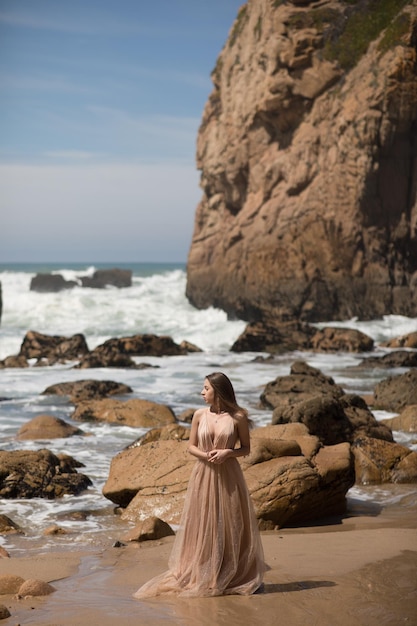 giovane donna in un vestito lungo che cammina sulla spiaggia vicino all'oceano.