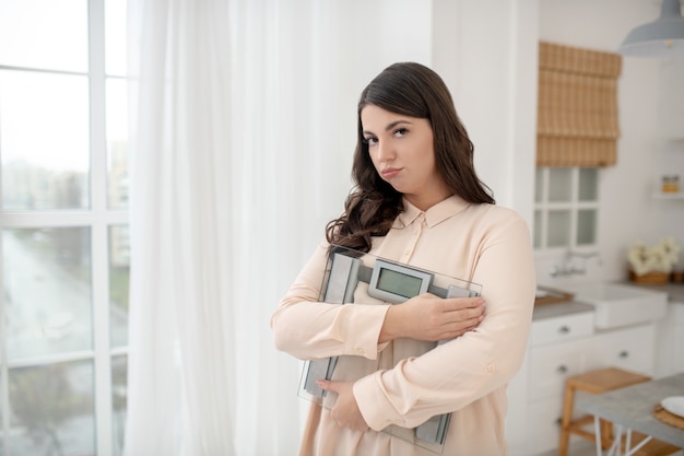 Giovane donna in una camicetta beige che tiene le bilance da pavimento e si sente stressata