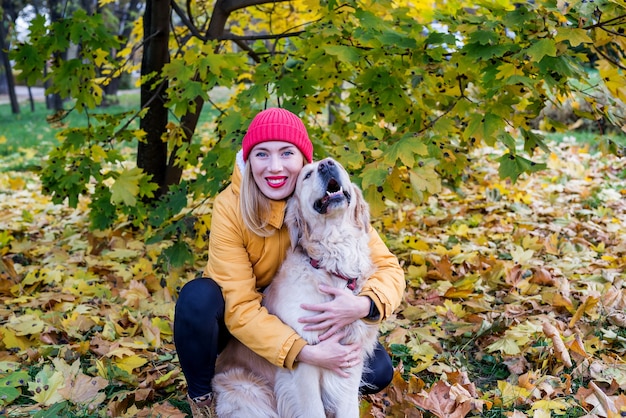 Giovane donna in una giacca gialla con il suo cane da riporto tra foglie autunnali gialle