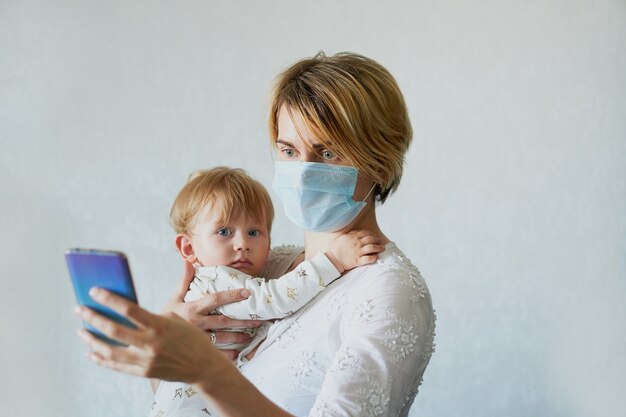 Giovane donna in una maschera medica con un bambino in braccio chiama al telefono