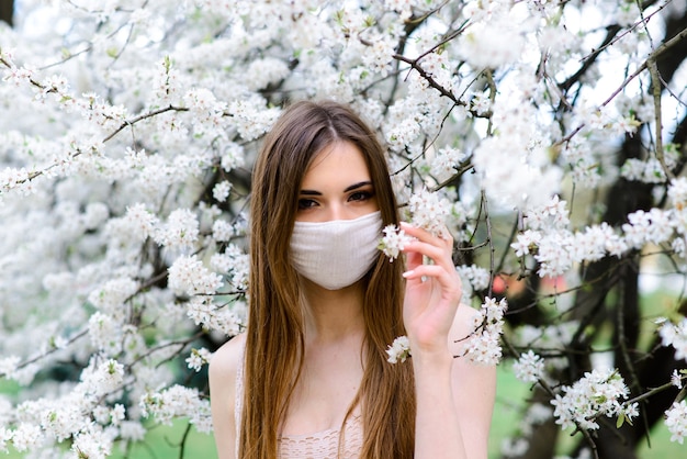 Giovane donna in una maschera medica sterile protettiva sul viso nel giardino di primavera.