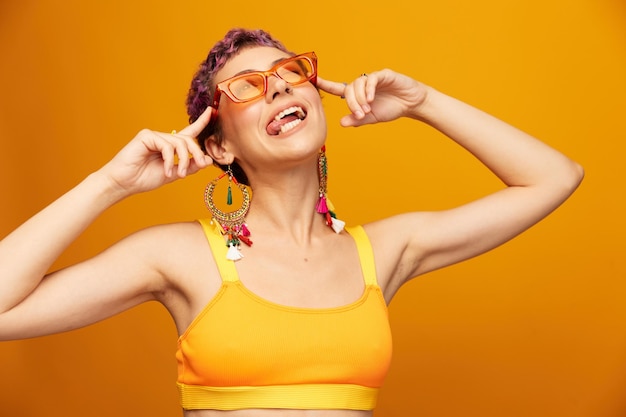 Giovane donna in una tuta da ginnastica gialla brillante con la pancia aperta e occhiali da sole su uno sfondo arancione sorridente foto di alta qualità