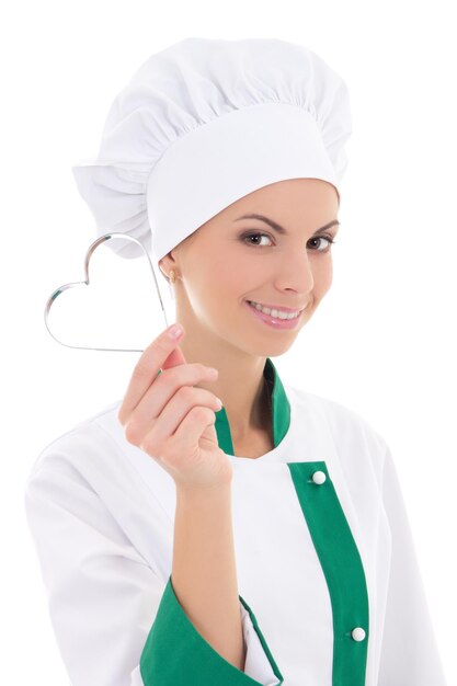 Giovane donna in uniforme da chef con tagliabiscotti a forma di cuore in metallo isolato su sfondo bianco