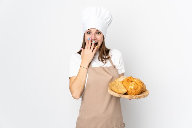 Giovane donna in uniforme del cuoco unico isolata su bianco con espressione facciale di sorpresa