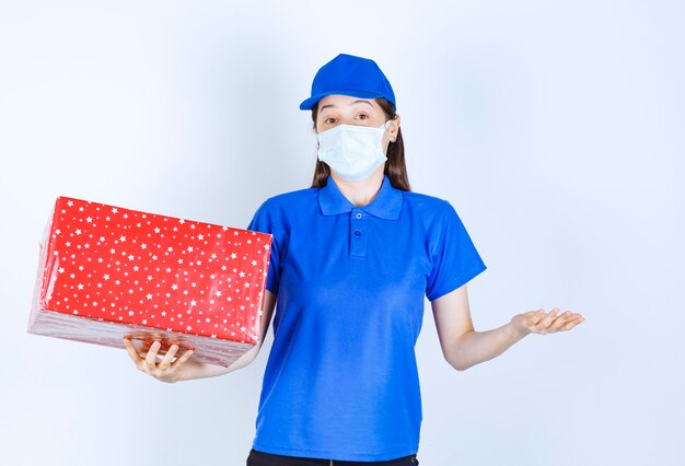 Giovane donna in uniforme e maschera medica che tiene il regalo di Natale.