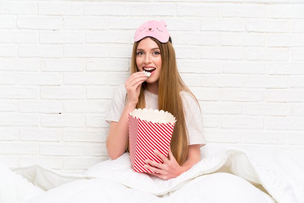 Giovane donna in vestaglia a letto tenendo popcorn