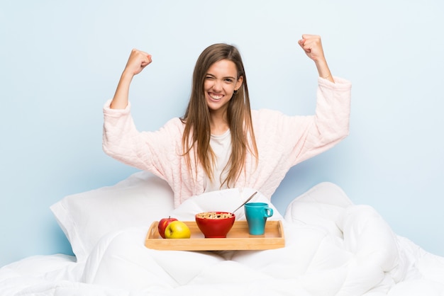 Giovane donna in vestaglia con colazione che celebra una vittoria