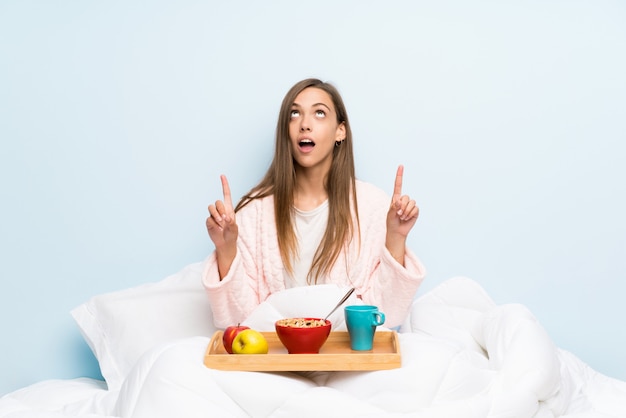 Giovane donna in vestaglia con colazione indicando con il dito indice una grande idea