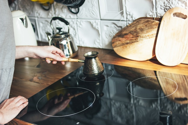 Giovane donna in vestito grigio che produce caffè nero naturale in vaso in cucina