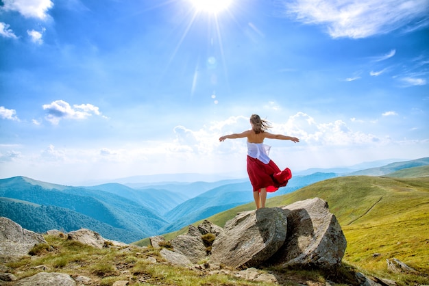 Giovane donna in vestito rosso che resta sulla cima della montagna