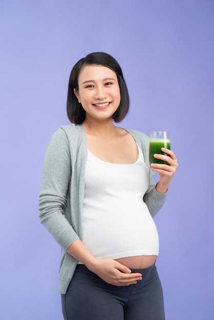 Giovane donna incinta abbastanza asiatica che beve succo verde