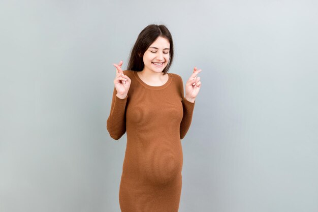 Giovane donna incinta allegra con le dita incrociate in attesa di una gravidanza isolata su uno sfondo colorato in studio stile di vita concetto di gravidanza