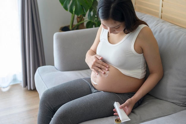 Giovane donna incinta che applica crema idratante sulla salute della pancia e sulla cura della gravidanza