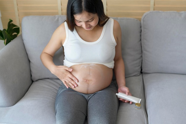 Giovane donna incinta che applica crema idratante sulla salute della pancia e sulla cura della gravidanza