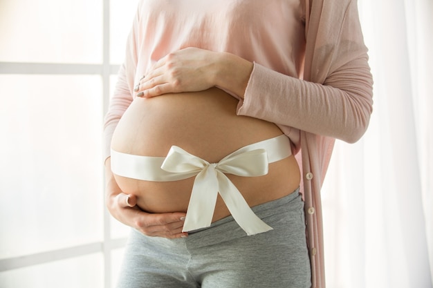 Giovane donna incinta che aspetta un genitore felice del bambino vicino alla finestra