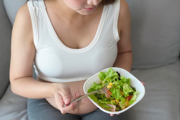 Giovane donna incinta che mangia insalata a casa assistenza sanitaria e gravidanza