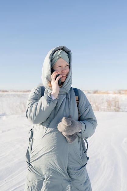 Giovane donna incinta che parla al telefono, all'aperto in inverno